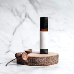 Minimalist product shot of an essential oil bottle on a wood slice with a marble background, ideal for skincare marketing.